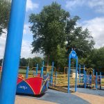 Children's playground equipment under a bright, cloudy sky with trees in the background.