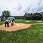 Baseball practice on a grassy field under an overcast sky with players and equipment visible.