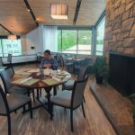 Modern restaurant interior with wooden ceiling, stone wall, and dining area.