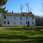 Historic white farmhouse under a clear blue sky with green lawn in the foreground.