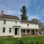 Historic white farmhouse with a porch under a blue, cloudy sky.
