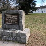 Stone monument honoring General Hugh Mercer, set on a grassy lawn near historic buildings.