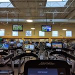 Indoor gym with cardio equipment, bright lighting, and high ceiling.