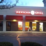 Mexican Grill storefront at dusk with red awnings and illuminated signage.