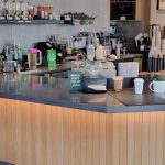 Modern cafe counter with wood paneling, espresso machine, and various coffee supplies.