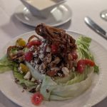 Salad topped with crispy bacon bits, nuts, and cherry tomatoes on a white plate.