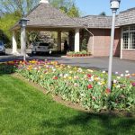 Sunny view of a brick building with a covered entrance and colorful spring flower beds.