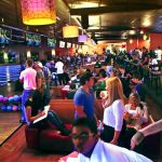 Crowded, dimly lit bar/lounge with a large screen displaying video content.