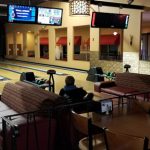 Bowling alley lounge area with seating, tables, and large video screens.