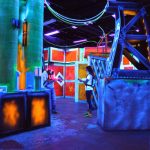 Nighttime club interior with vibrant neon lighting, futuristic decor, and people socializing.