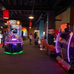 Arcade hall with colorful games, including a prize counter and ride simulators.