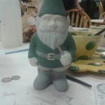 Ceramic gnome figurine on a white table with art supplies and yellow bowl.