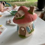 Clay model of a pink and white mushroom house on a white table outdoors.