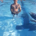 Man smiling in a bright outdoor swimming pool with lane markers visible.