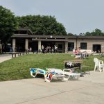 Outdoor gathering area with green lawn, modern building, and people relaxing on lounge chairs.