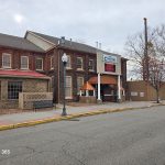 Brick building with commercial storefront on a street under an overcast sky.