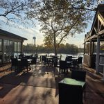 Outdoor dining area overlooking a body of water under autumn trees.