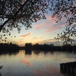 Sunset over a calm lake, framed by silhouetted trees and colorful clouds.