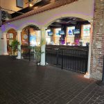 Brick courtyard leading to an arched entrance of a venue with interior lighting.