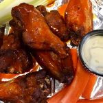 Glazed chicken wings and orange slices on a foil-lined baking sheet.