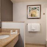 Bathroom vanity with granite countertop, mirror, and framed art on a tiled wall.
