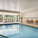 Indoor swimming pool area with lounge chairs and large windows overlooking greenery.