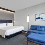 Modern hotel room with a large bed, blue sofa, and contemporary artwork.