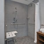 Modern gray tiled shower with rainfall head, handheld spray, and white curtain.