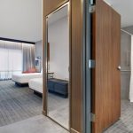 Modern hotel room interior showing a bedroom area and bathroom entrance with wood-paneled doors.