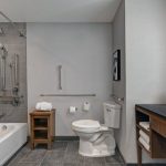 Modern hotel bathroom with white tub, toilet, and dark wood vanity.