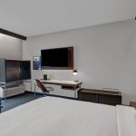 Modern hotel room with large bed, TV, and minimalist decor.