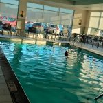 Swimmer in a bright, indoor swimming pool overlooking an outdoor area.