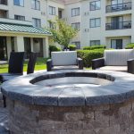 Stone fire pit surrounded by comfortable outdoor seating in a modern apartment complex courtyard.
