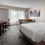 Modern hotel room with a queen bed, sofa, and large window view.