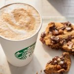 Starbucks latte in a cup next to chocolate chip cookies on a white plate.