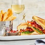 Golden fries and a grilled sandwich served with white wine on a platter.