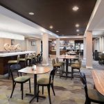 Modern hotel lobby with seating areas, dark ceiling, and view into a bar area.