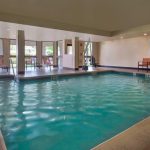 Indoor swimming pool with blue water, surrounded by lounge chairs and a bright atrium area.