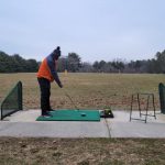 Golfer practices putting on a green in an outdoor driving range setting.