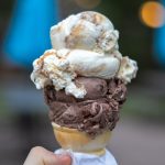 Scoop of chocolate and vanilla ice cream in a cone, held by hand outdoors.