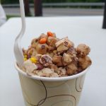Dessert in a yellow cup, featuring crumbled cookies and sweet toppings.