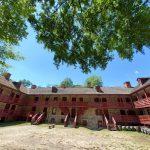 Historic brick building with wooden balconies under a bright, leafy canopy.