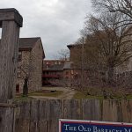 Historic stone barracks and wooden fence under an overcast sky.
