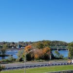 Blue sky over a river with a bridge, trees, and highway in the foreground.