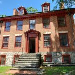 Historic red brick building with stone foundation and multiple windows under a blue sky.