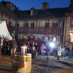 Nighttime gathering outside a historic brick building with tents and barrels.