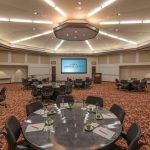 Large, well-lit conference room with round tables set up for a corporate event.