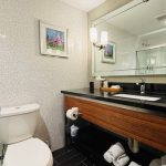 Modern bathroom with white toilet, dark vanity, and large mirror.