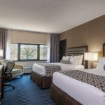 Two hotel beds in a room with modern decor, large window view of trees.