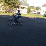 Cyclist on a bicycle rides down an asphalt street with houses and trees in the background.